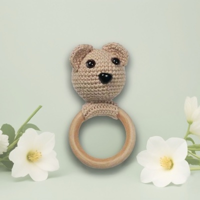 Chocalho para bebé em forma de urso de croché com anel de madeira em fundo verde claro e flores brancas