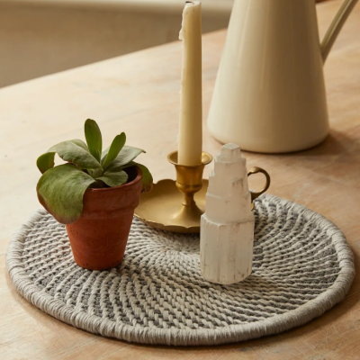 Base redonda têxtil com castiçal, vela, planta suculenta e escultura sobre mesa de madeira