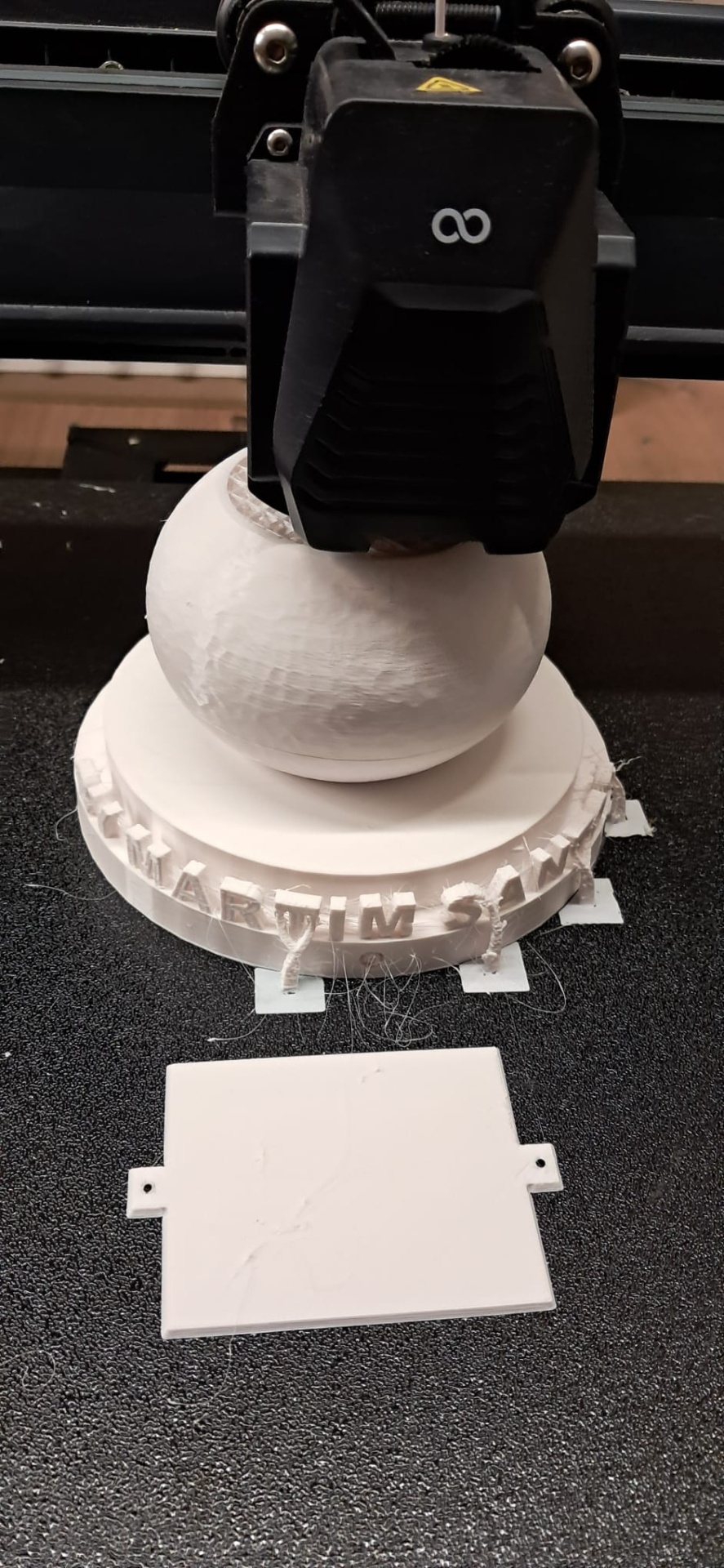 Impressora 3D a imprimir objeto branco com base circular e texto em relevo