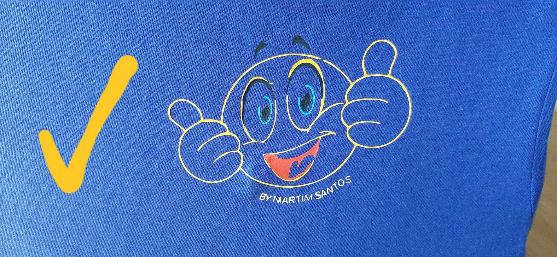 Camisola azul com desenho de sorriso amarelo e texto BY MARTIM SANTOS.