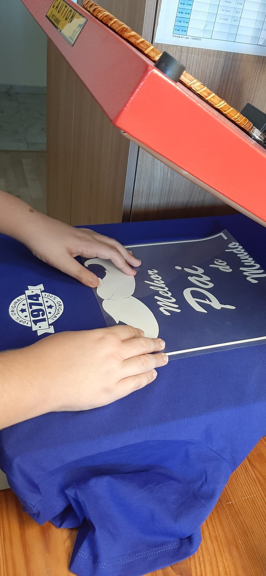 T-shirt azul com estampa branca e prensa térmica vermelha numa mesa de madeira