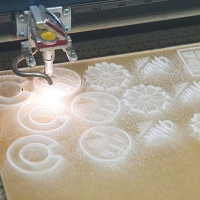 Máquina laser a gravar formas circulares e florais num material branco sobre base castanha