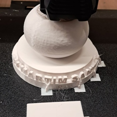 Impressora 3D a imprimir objeto branco com base circular e texto em relevo