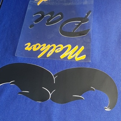 T-shirt azul com texto 100% ORIGINAL 1974 e bigode preto, com autocolante transparente com texto em amarelo e preto