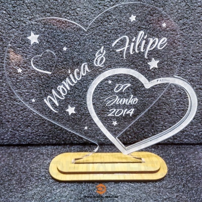 Duas formas de coração em acrílico transparente com texto branco gravado sobre base de madeira.