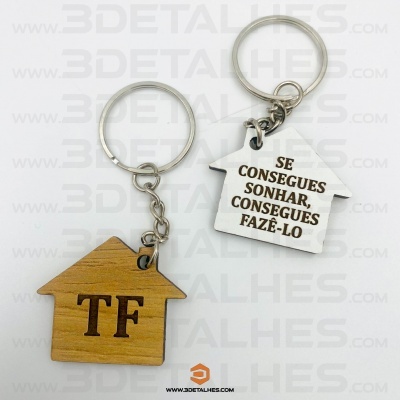 Dois porta-chaves em forma de casa, um de madeira com 'TF' e outro de metal com texto motivacional.