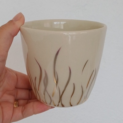 Caneca de cerâmica bege com linhas onduladas castanhas e douradas