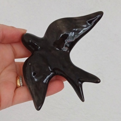 Escultura preta de pássaro em cerâmica sendo segurada por uma mão