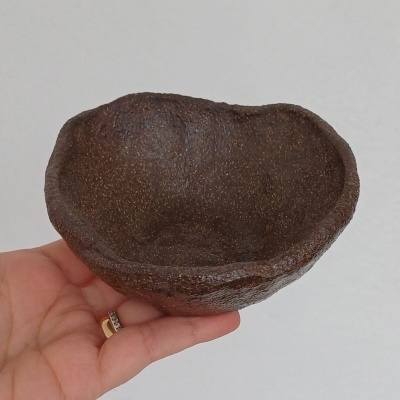 Taça pequena castanha escura com textura irregular, segurada por uma mão