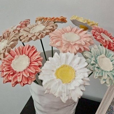Arranjo de flores artificiais coloridas num vaso branco sobre mesa escura.