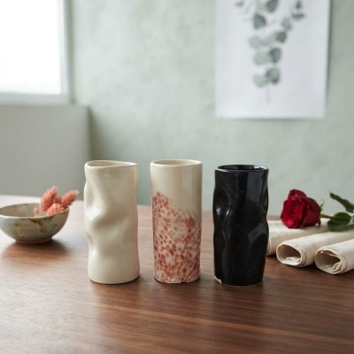 Três copos de cerâmica ondulada em creme, creme com manchas castanhas e preto sobre mesa de madeira