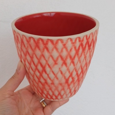 Vaso de cerâmica vermelho com padrão de losangos, visto de perto na mão.