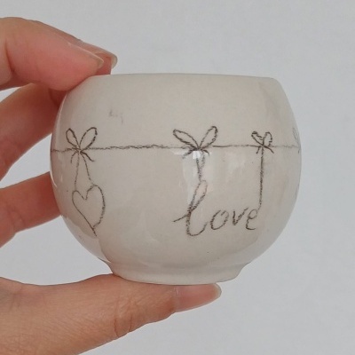 Vaso pequeno branco com desenhos a preto de corações, laços e a palavra 'love'