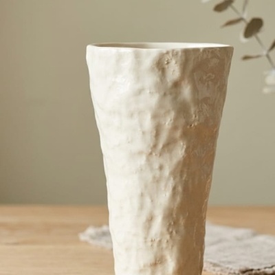Vaso de cerâmica branco com textura irregular sobre mesa de madeira.