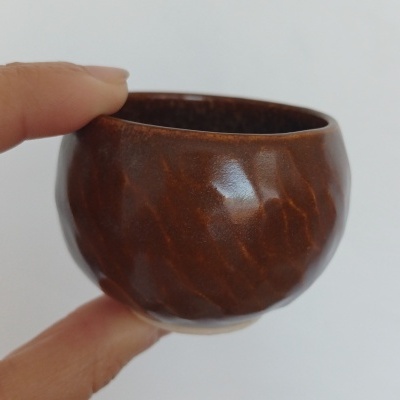 Pequena taça cerâmica castanha com textura ondulada na mão