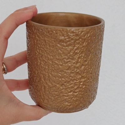Copo dourado texturizado segurado por uma mão