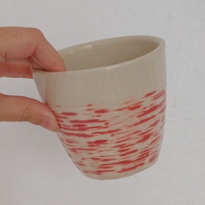 Caneca branca com padrão vermelho, segurada por mão, fundo branco