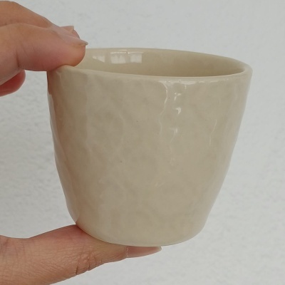 Copo pequeno em cerâmica creme com textura irregular e acabamento brilhante