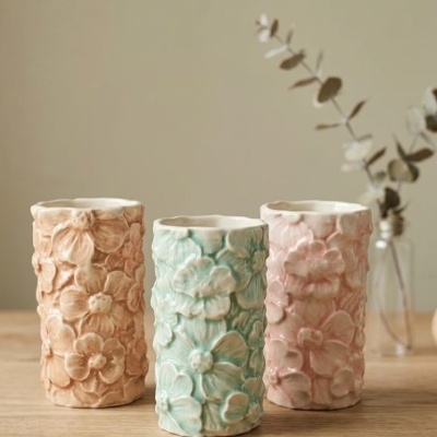 Três vasos de cerâmica com flores em relevo em cores pastel sobre mesa de madeira.