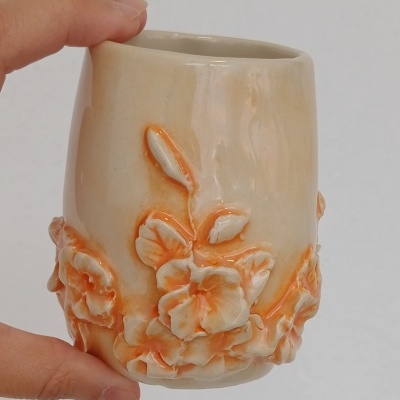 Copo de cerâmica bege com flores em relevo laranja e creme