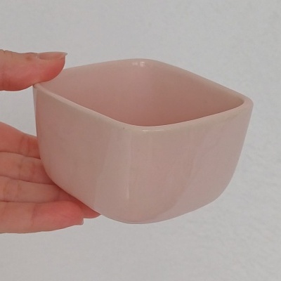 Recipiente quadrado de cerâmica rosa claro liso e brilhante segurado por mão