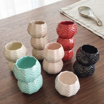 Vasos cerâmicos pequenos com padrão zig-zag em várias cores sobre mesa de madeira clara.