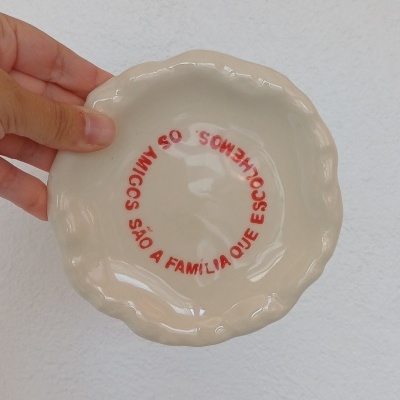 Prato pequeno cerâmico creme com texto vermelho em círculo no centro e bordas onduladas