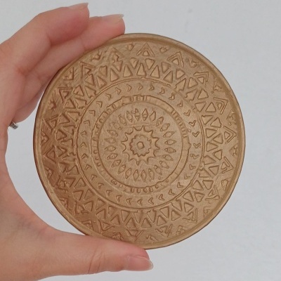 Disco redondo castanho claro com padrão geométrico gravado segurado por uma mão
