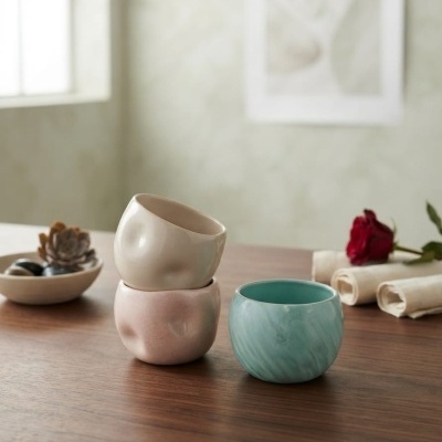 Três vasos cerâmicos coloridos sobre mesa de madeira com decoração ao fundo