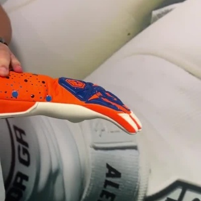 Pessoa a vestir luva de guarda-redes laranja com detalhes azuis e brancos