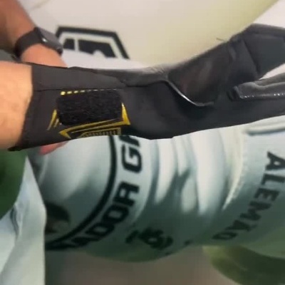 Pessoa a vestir luvas desportivas pretas com detalhes dourados e ajustar tira no pulso.