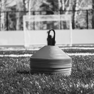 Cones de treino empilhados sobre relvado artificial num campo de futebol