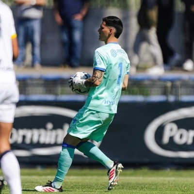 Guarda-redes de futebol em equipamento verde-água segurando bola no campo