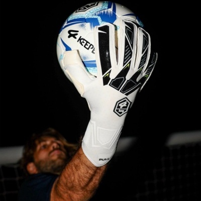 Luvas de guarda-redes brancas segurando bola de futebol azul e branca em fundo escuro