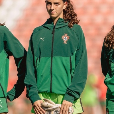 Casaco desportivo verde com logótipos da Puma e seleção de Portugal, usado por pessoa com luvas de guarda-redes num estádio.