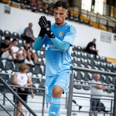Jogador de guarda-redes de futebol com equipamento azul claro e luvas pretas num estádio.
