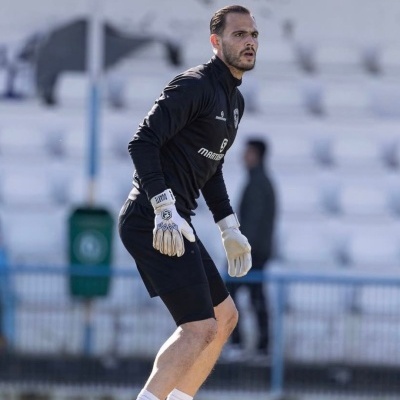 Jogador de futebol com roupa preta e luvas brancas em campo de futebol