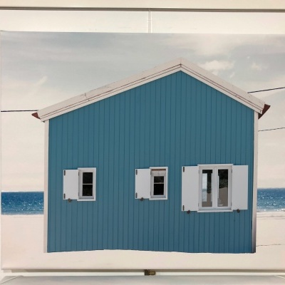Casa azul com janelas brancas em cenário de praia com mar e céu nublado.