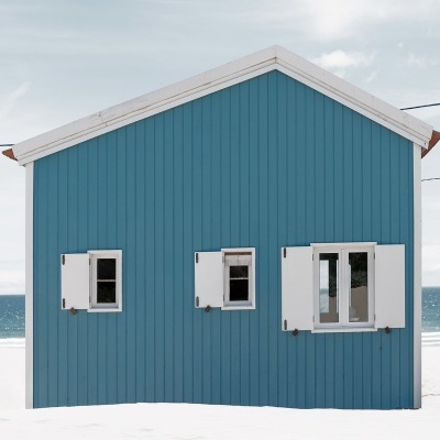 Casa de praia azul com janelas brancas e mar ao fundo