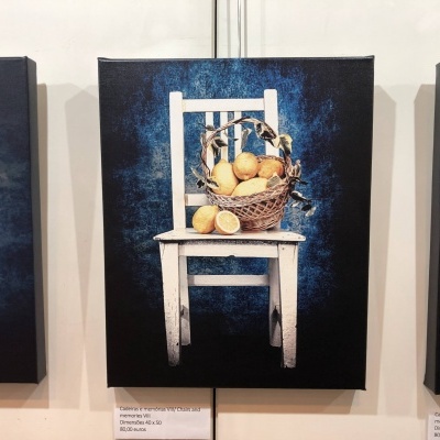 Quadro com cadeira branca, cesta de vime e limões exposto numa galeria