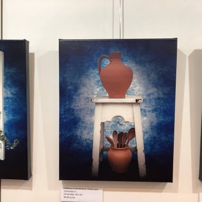 Tela artística com jarra de barro sobre banco branco com colheres em vaso de barro sobre fundo azul