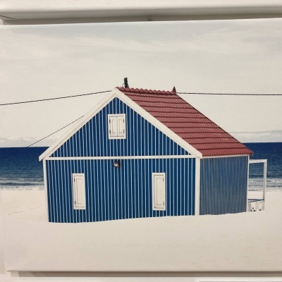 Quadro de casa azul com riscas brancas e telhado vermelho junto à praia