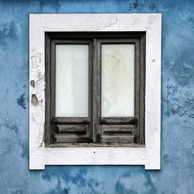 Janela de madeira antiga com vidro fosco numa parede azul desbotada.