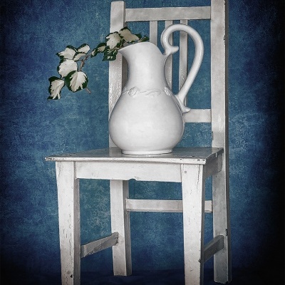 Cadeira branca de madeira com jarro branco contendo ramo com folhas