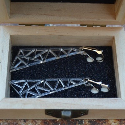 Brincos triangulares metálicos prateados em caixa de madeira na mesa metálica envelhecida