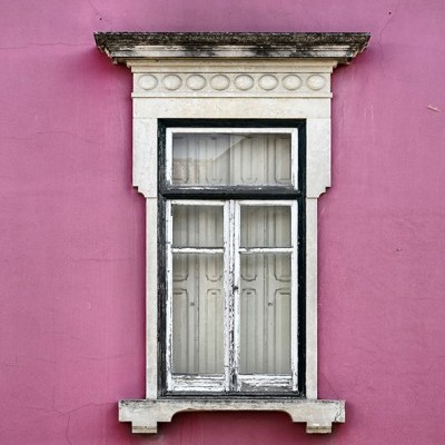 Janela branca velha com moldura preta em parede rosa com ornamentos em pedra branca