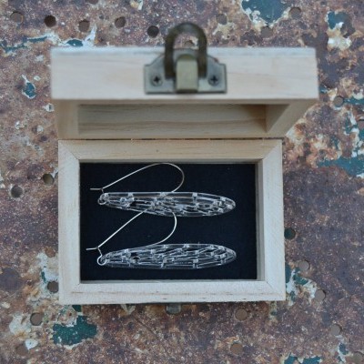 Caixa de madeira aberta com dois brincos prateados dentro