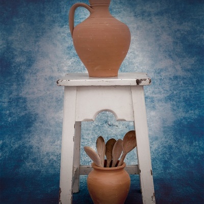 Dois jarros de barro castanho com colheres de madeira em banco branco com fundo azul.