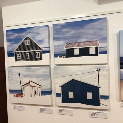 Quadros com imagens de casas à beira-mar em azul, branco e vermelho numa parede branca.
