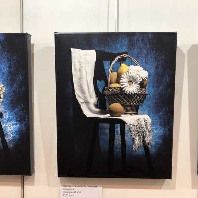 Pintura de um banco preto com toalha branca, cesta de vime com pêras e flores, fundo azul escuro